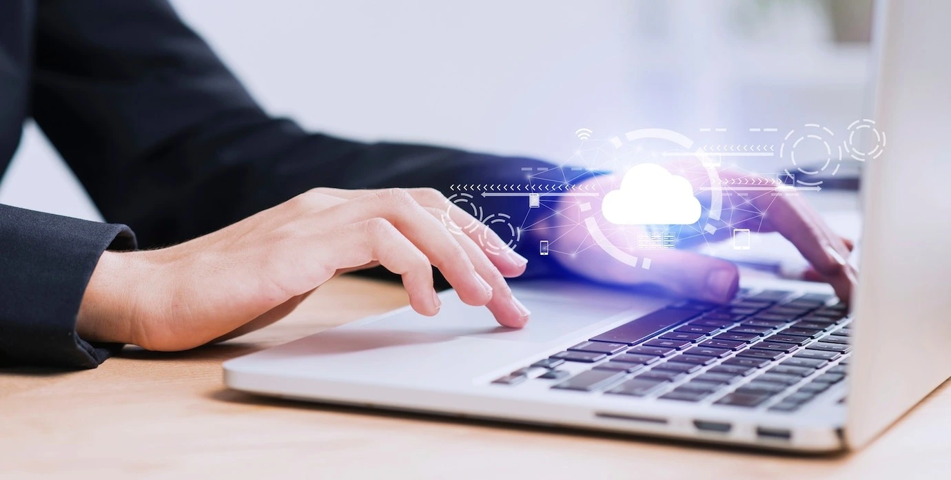 Professional using a laptop with a graphic overlay of a cloud and digital icons, representing cloud computing or cloud services in a business context.